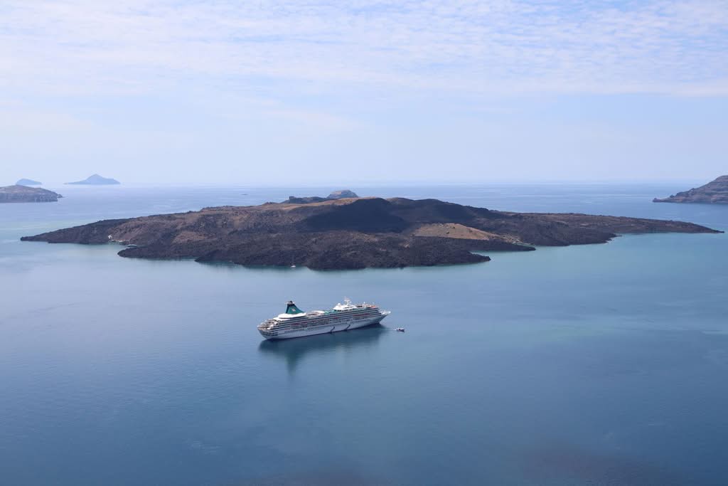 A cruise ship navigates near the volcanic island of Nea Kameni near Santorini, Greece
