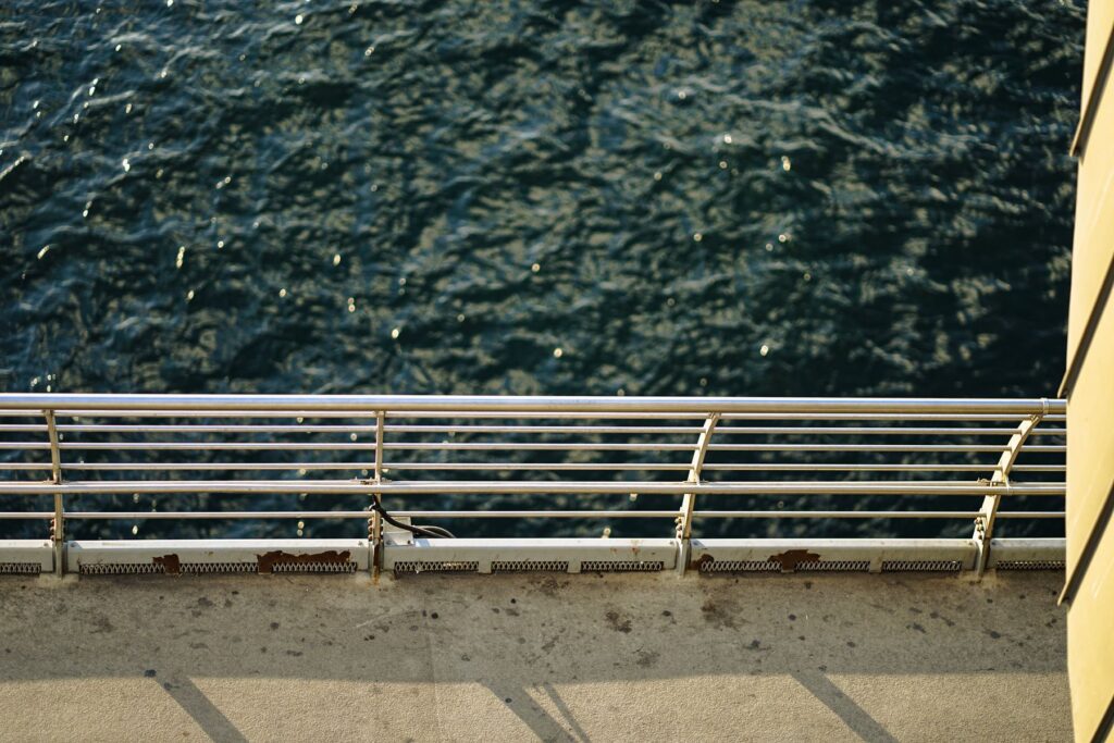 Perspective from a ship's deck, showcasing the ocean and metal railing in soft daylight