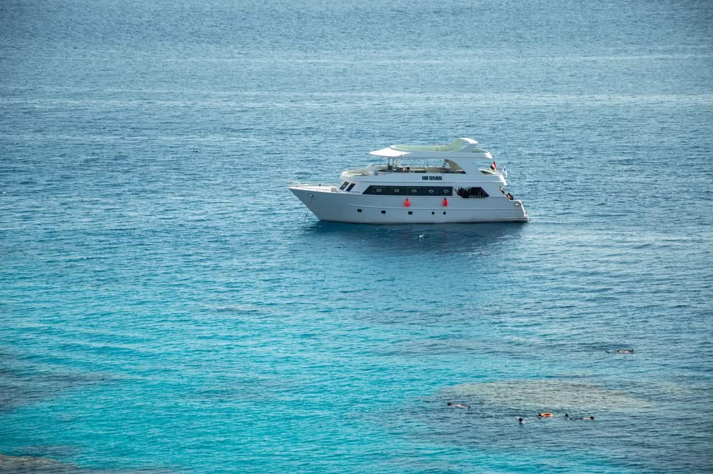 A luxurious white yacht on clear blue sea with snorkelers nearby, taken from an aerial view