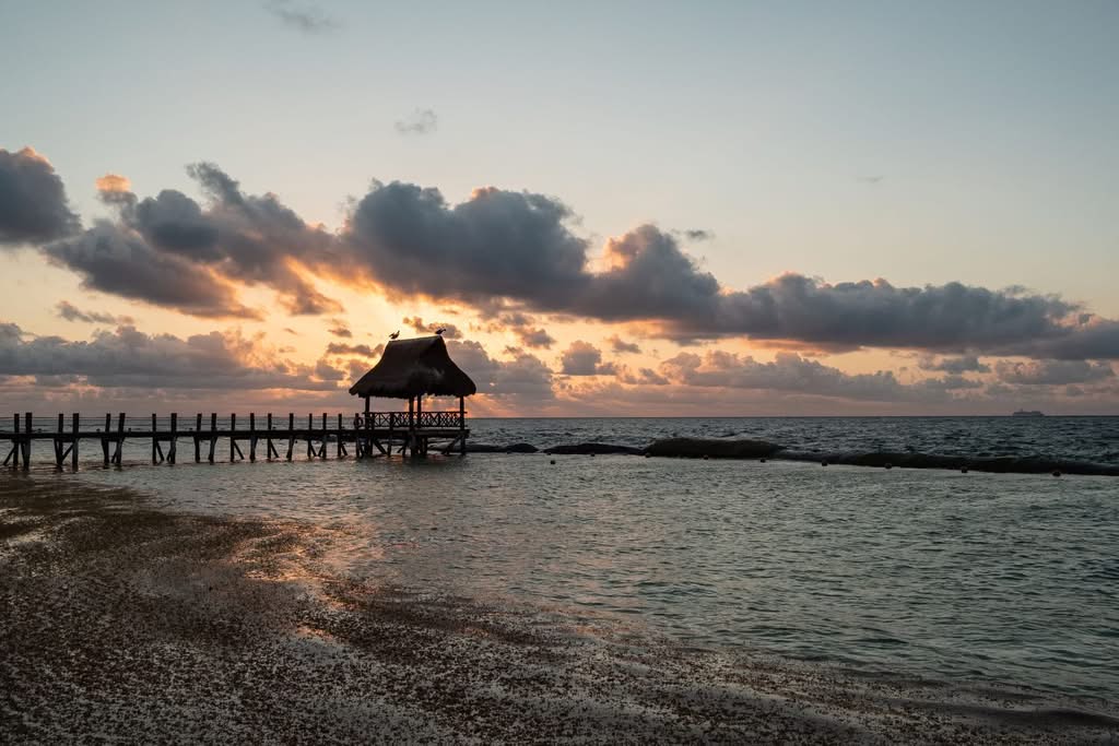 Captivating sunrise at Playa del Carmen with a pier extending into the ocean, under dramatic clouds