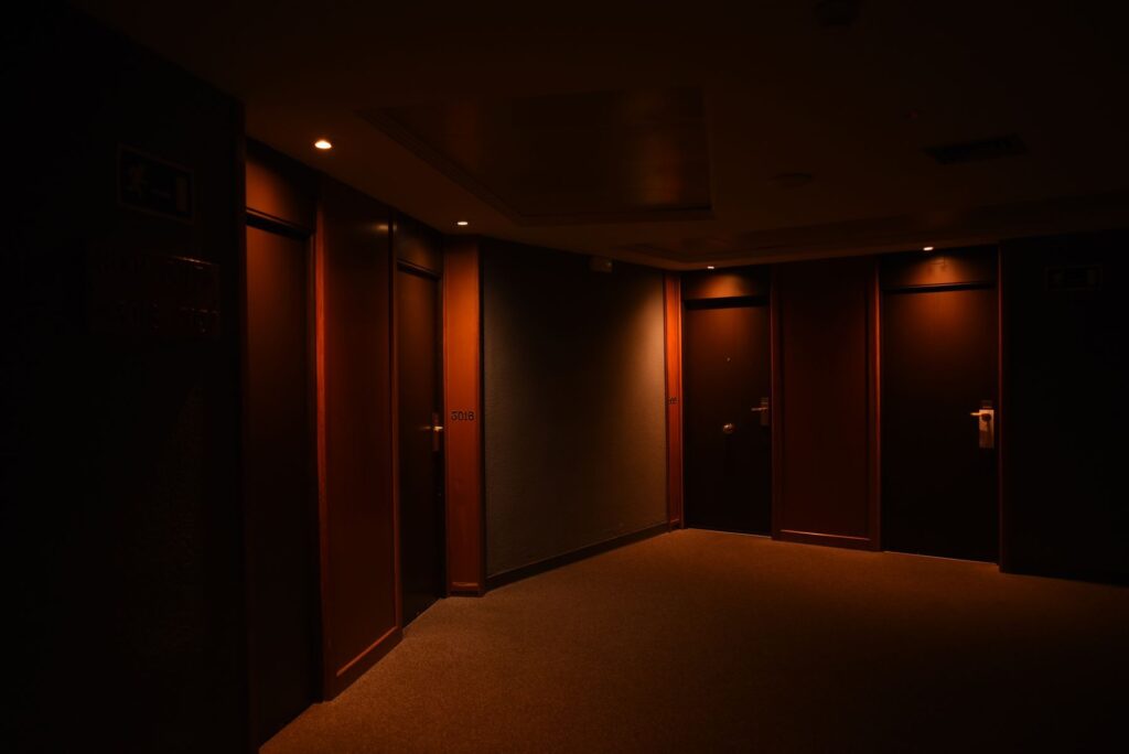 A dark, quiet hotel corridor featuring multiple closed wooden doors and soft lighting