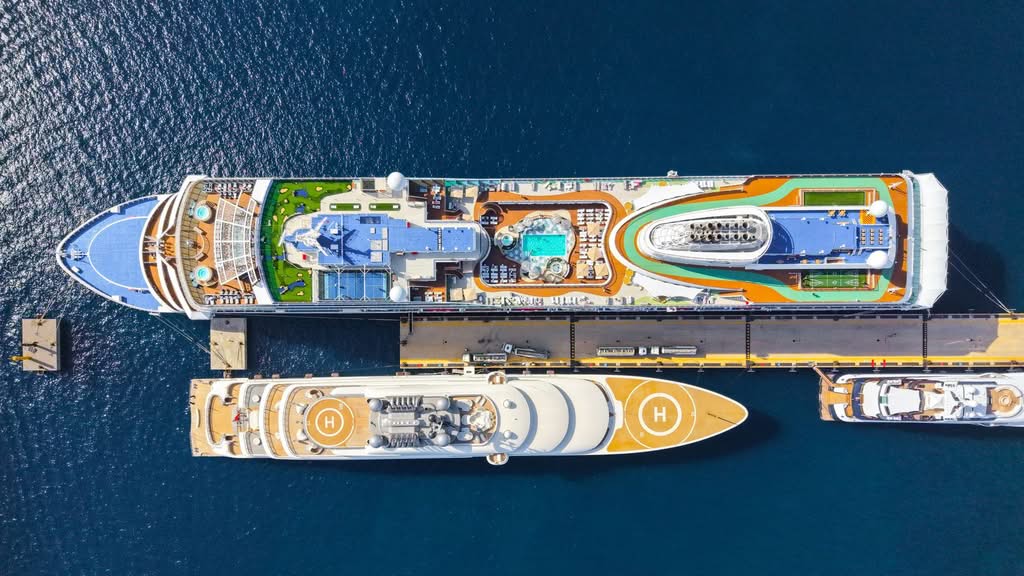 Top-down view of two luxurious cruise ships moored at a sunny port, showcasing pools and helipads