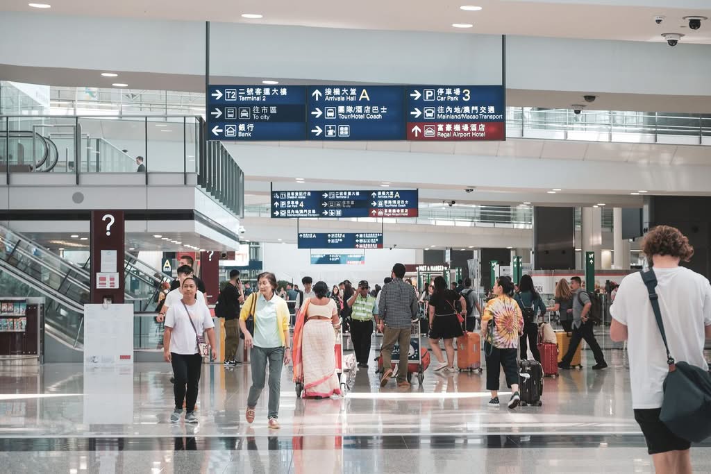 Crowded Hong Kong airport terminal with diverse passengers and informative signage