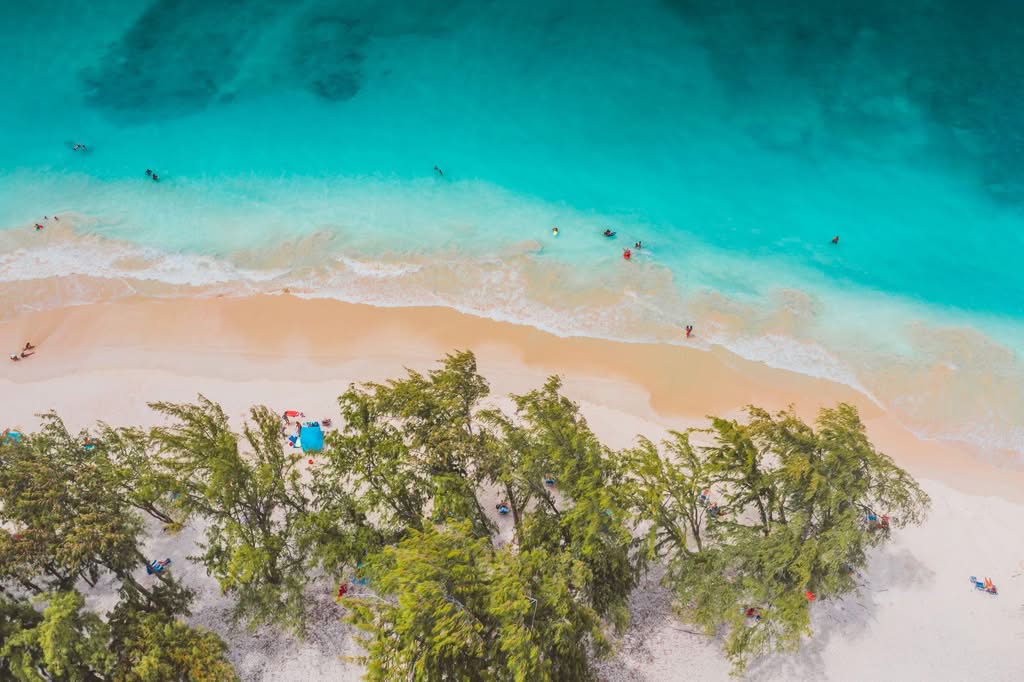 A stunning aerial shot of a tropical beach with vivid turquoise waters, sandy shore, and lush greenery