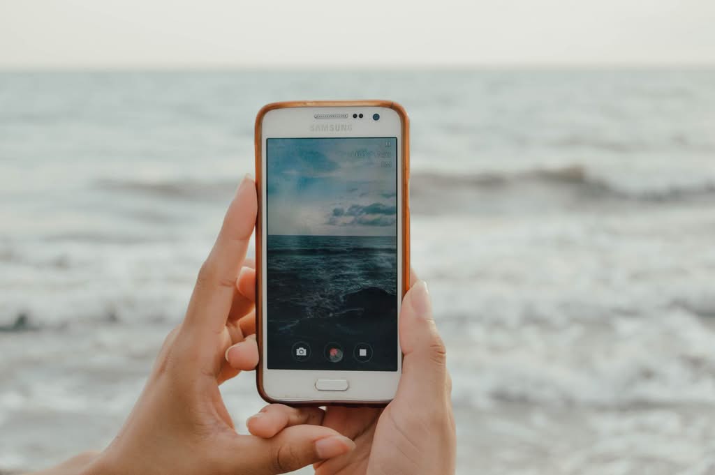 Hands holding a smartphone taking a picture of the ocean. Perfect for technology and travel themes