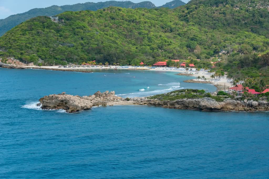 Explore a serene tropical coastline with vibrant green hills and tranquil blue waters, ideal for a summer getaway